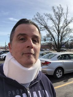 a man with a cast on his neck standing in front of parked cars