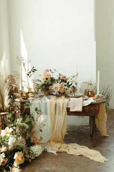 a table with flowers and candles on it in front of a white wall next to a rug