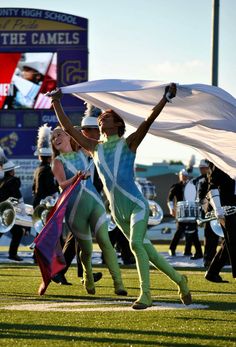 two women in bodysuits are dancing on the field with their hands up and one is holding a flag