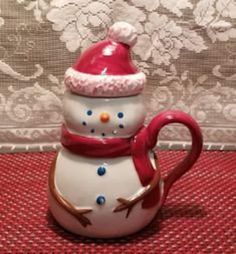 a ceramic snowman mug with a red hat and scarf on it's head