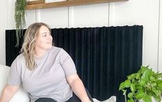 a woman sitting on top of a white couch next to a potted green plant