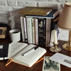 an open book sitting on top of a wooden desk next to a lamp and telephone