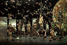 a group of people standing on top of a stage with birds flying over them in the air