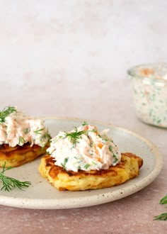 two crab cakes on a plate with dill sprinkled on top and another dish in the background