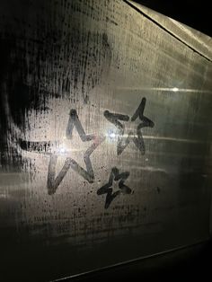 some writing on the side of a train window with rain drops falling down and stars painted on it