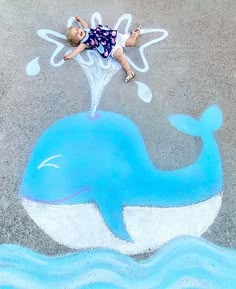 a little boy laying on top of a blue whale drawn in chalk with white paint