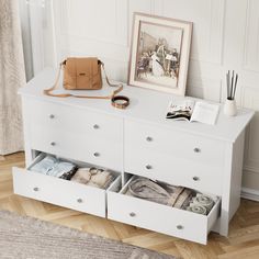 a white dresser with two drawers and a purse on it's top shelf next to a framed photograph