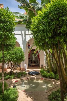 an outdoor pool surrounded by trees and plants in the middle of a courtyard with a fountain