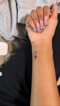 a woman's hand with a small tattoo on her left wrist and two hearts in the middle