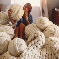 a woman sitting on the floor surrounded by giant balls of yarn