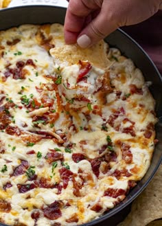 a person dipping a piece of pizza into a skillet with tortilla chips