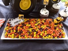 a table topped with lots of cupcakes and candy next to a monster truck