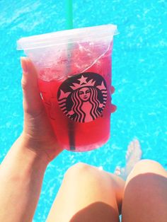 a person holding up a drink in front of a swimming pool