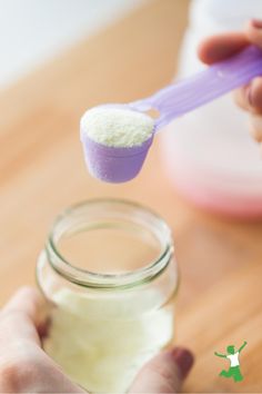 a person holding a spoon over a jar filled with white sugar and lavender powder on a wooden table