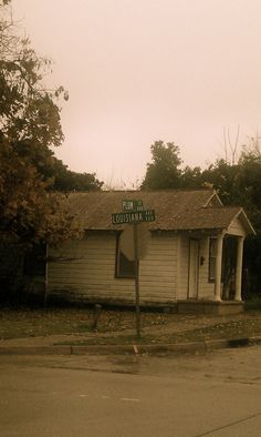 an old white building with a street sign in front of it and trees behind it