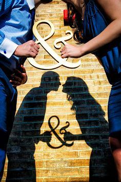 two people standing next to each other in front of a brick wall with the word & amp on it