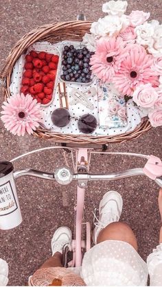 a person riding a bike with flowers and berries in the basket next to their feet