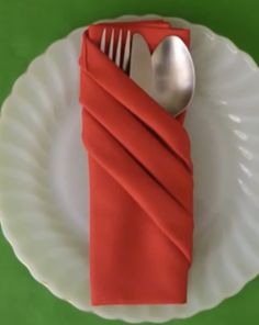 a fork and knife wrapped in red cloth on a white plate with a green background