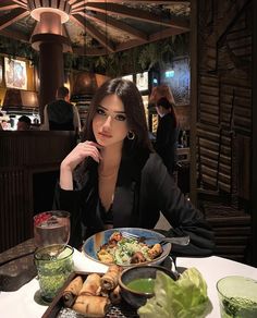 a woman sitting at a table in front of a plate of food with vegetables on it