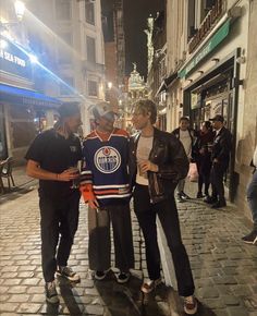 three men are standing on the street talking to each other while one man is wearing an edmonton oilers jersey