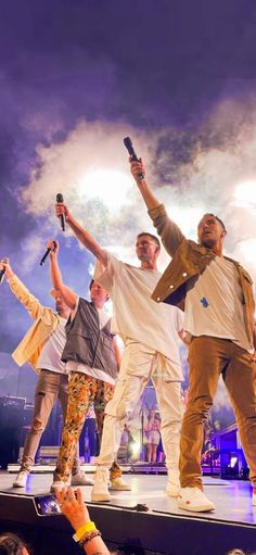 some people are standing on a stage with their arms in the air and one is holding a microphone