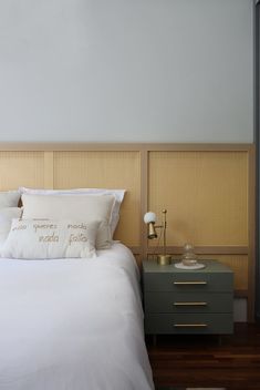 a bed with white sheets and pillows next to a night stand on a wooden floor