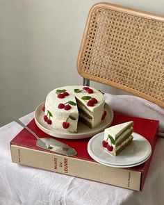 a cake sitting on top of a red box next to a slice of cake with cherries