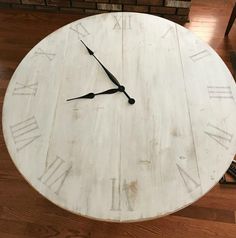 a white clock sitting on top of a wooden table next to a brick wall with roman numerals