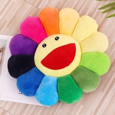 a multicolored flower shaped pillow sitting on top of a wooden floor next to a plant