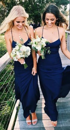 two bridesmaids walking down a wooden bridge holding bouquets in their hands and laughing