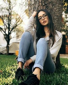 a woman sitting in the grass next to a tree