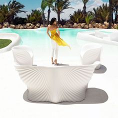 a woman standing on top of a white bench next to a pool with palm trees in the background