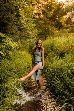 a woman in a green dress is sitting on the edge of a stream and smiling