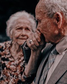 an older man and woman standing next to each other with their hands on their chins