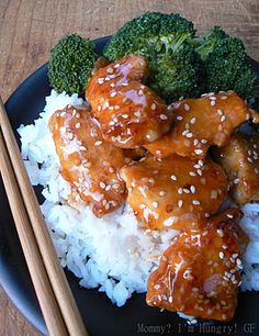 a black plate topped with chicken and broccoli next to chopsticks on top of rice