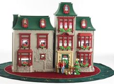 two people standing in front of a doll house with christmas wreaths on the windows