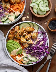 two bowls filled with chicken and veggies on top of a wooden table next to silverware