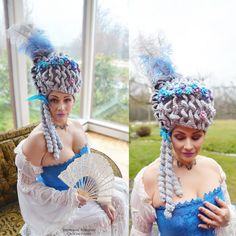 a woman in a blue dress holding a fan and wearing a crochet hat