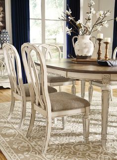 a dining room table with chairs and a vase filled with flowers on top of it