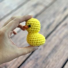 a small yellow crocheted ducky sitting on top of a wooden table next to a person's hand