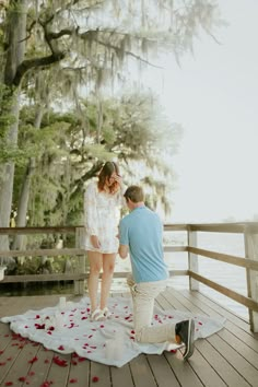 a man kneeling down next to a woman on top of a wooden deck with rose petals