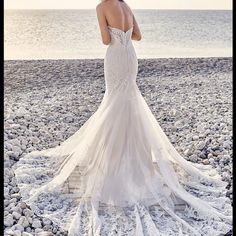 a woman in a wedding dress standing on rocks near the ocean with her back to the camera