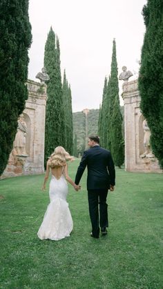 a bride and groom holding hands walking through an archway way in the middle of a field