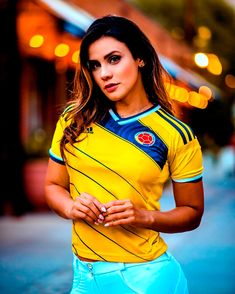 a woman in yellow shirt and blue pants posing for a photo with lights behind her