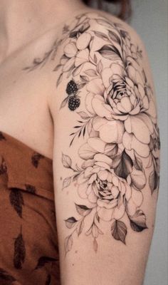 a woman's shoulder with flowers and leaves tattooed on her left arm, in black and white