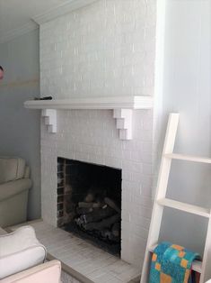 a man standing next to a fireplace in a living room with white walls and a ladder