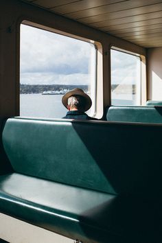 a man in a hat sitting on a train looking out the window at the water