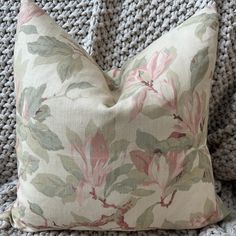 a close up of a flowered pillow on a couch with a knitted blanket