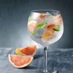 a glass filled with water and fruit on top of a table next to a slice of grapefruit