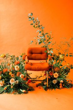 an orange chair surrounded by flowers and greenery in front of an orange wall,